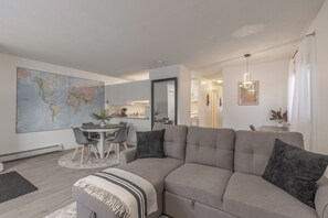 Un saló modern amb un sofà modular, una taula de dinar amb caires, un mapa mundial gran a la paret i una cuina al fons.