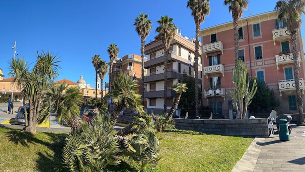 A sunny urban square with palm trees, a fountain, and multi-story buildings with balconies. - ML in sea promenade (Chiavari)