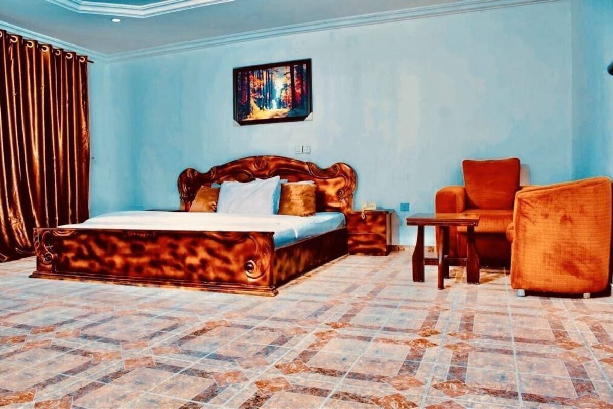 Une chambre avec un grand lit, une chaise, une petite table et un tableau accroché au mur.