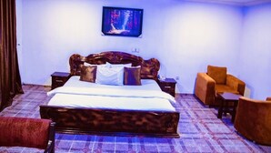 A bedroom with a large bed, a television on the wall, and a seating area with two chairs. - E-Gold Luxury Hotel (Abuja)