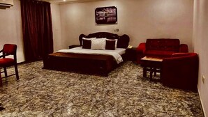 A hotel room with a large bed, two red armchairs, a small table, and a carpeted floor. - E-Gold Luxury Hotel (Abuja)
