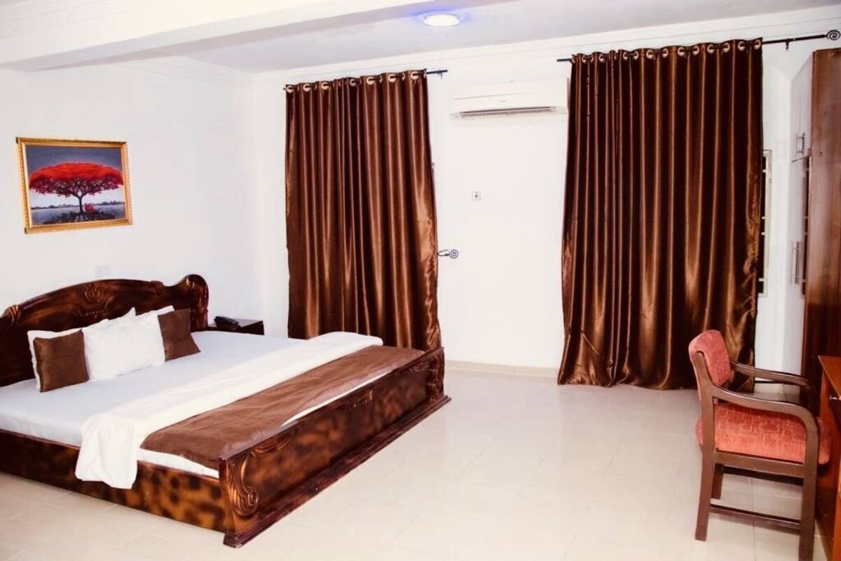 Une chambre à coucher avec un lit, des rideaux, une chaise et un tableau accroché au mur.