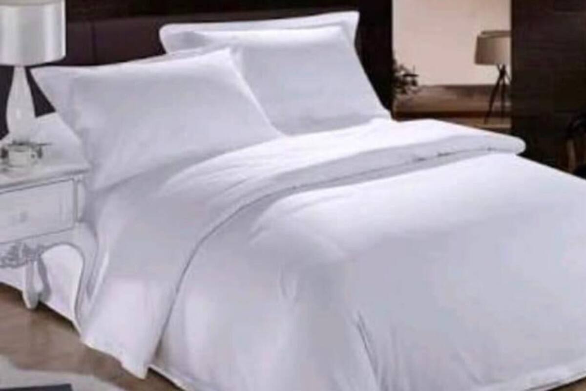 Un lit bien fait, avec du linge de lit blanc, dans une chambre d'hôtel.