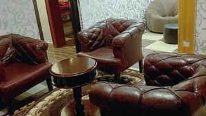 A living room with leather armchairs, a round coffee table, and a patterned rug. - E-Gold Luxury Hotel (Abuja)