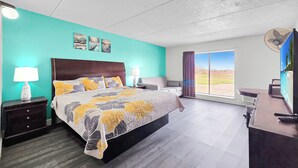 A bedroom with a bed, nightstands, a desk, a chair, a TV, and a large window with a view.
