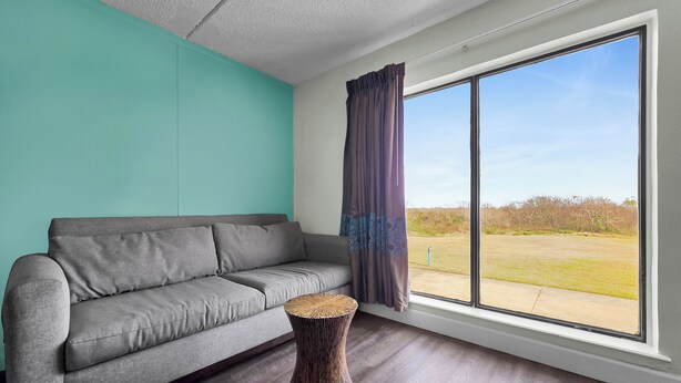 A modern living room with a grey sofa, a round wooden side table, and a large window with curtains.