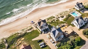 An aerial view of a coastal property with multiple houses, a swimming pool, and a beach.