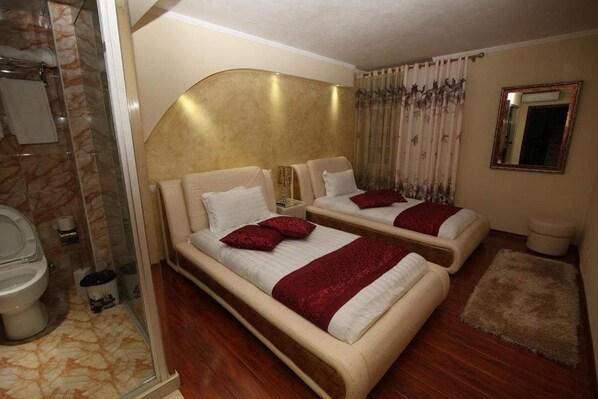 A hotel room with two beds, a shower, a toilet, and a mirror.
