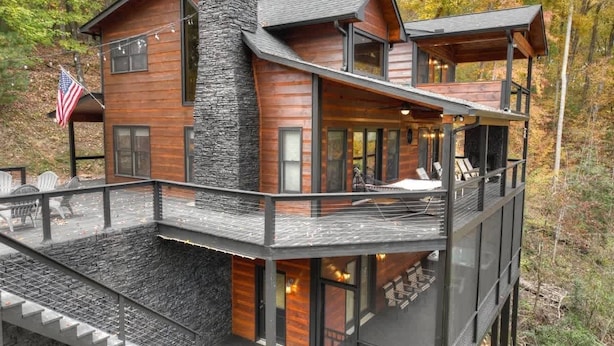 Une cabane en bois à plusieurs niveaux, dotée d’une cheminée en pierre, d’un espace extérieur aménagé et d’un drapeau.