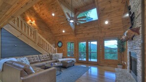 Un vaste salon doté d’un plafond en bois, d’une cheminée en pierre, d’un grand canapé et d’un escalier menant à un niveau supérieur.