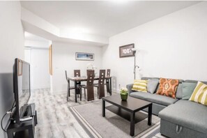Una sala de estar moderna con un sofá gris, una mesa de centro, un televisor sobre un mueble, una mesa de comedor con sillas y un cuadro enmarcado en la pared.