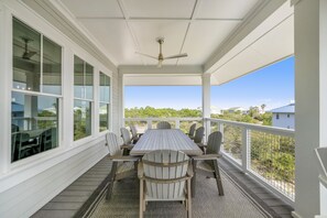 A covered outdoor dining area with a table and chairs, large windows, and a view of the surrounding landscape.