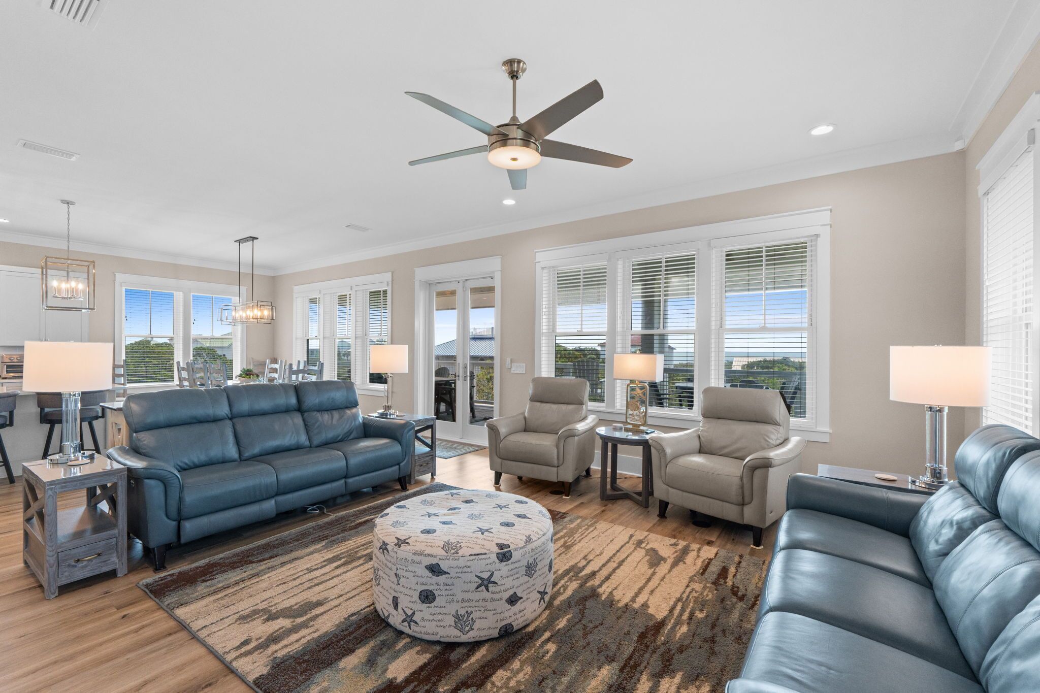 A spacious living room with a blue sofa, two armchairs, a coffee table, and a ceiling fan.
