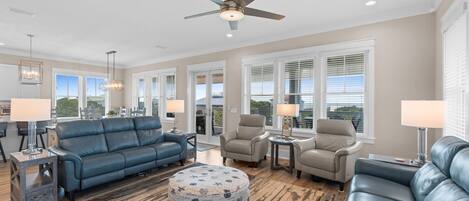 A spacious living room with a blue sofa, two armchairs, a coffee table, and a ceiling fan.