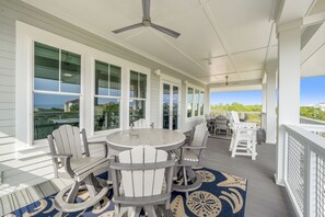 A covered outdoor area with a round table and chairs, large windows, and a ceiling fan.