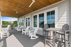 En overdækket terrasse med hvide Adirondack-stole og borde, store vinduer og et træloft.