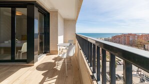 A balcony with a wooden floor, white chairs, and a glass door leading to a room. - Patacona Sunrise Duplex I. Wifi + parking + pool + paddle (Alboraya)