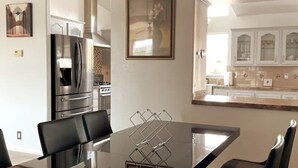 A modern kitchen with stainless steel appliances, a dining table with chairs, and a decorative vase on the wall. - SERENITY AWAITS HILL WINE Co#2 (Temecula)