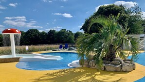A swimming pool with a water slide, palm trees, and a fenced area with lounge chairs. - Owls Nest (Wimborne)