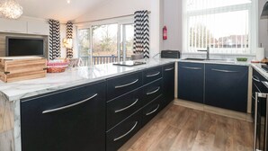 A modern kitchen with a large island, black cabinets, and a large window providing a view of the outdoors. - Owls Nest (Wimborne)