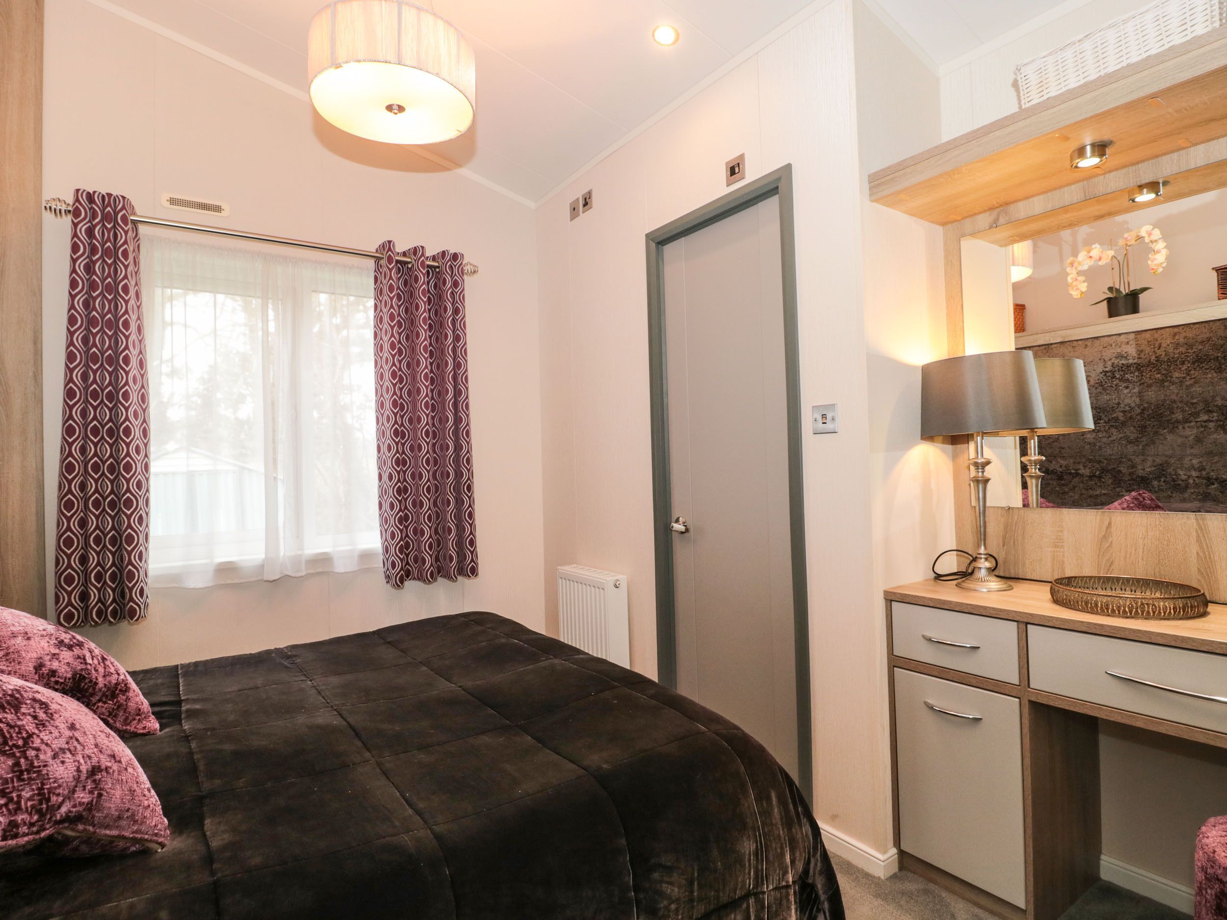 Un dormitorio con cama, cómoda, espejo y ventana con cortinas.