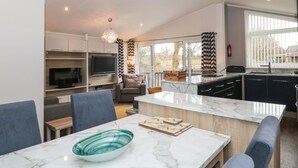 A modern kitchen with a marble countertop, a built-in TV, and a dining area with a blue chair and a glass bowl. - Owls Nest (Wimborne)