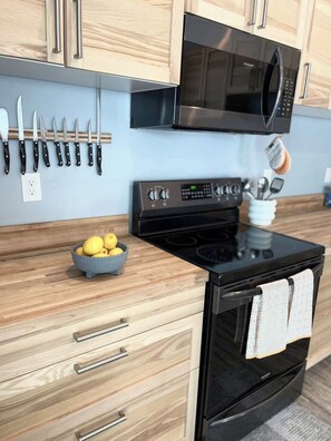 A kitchen with wooden cabinets, a black microwave, a stove, and a bowl of lemons. - Dune View at Silver Lake (Mears)
