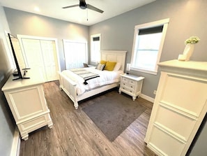A bedroom with a bed, bedside tables, a nightstand, a dresser, a ceiling fan, and a window. - Dune View at Silver Lake (Mears)