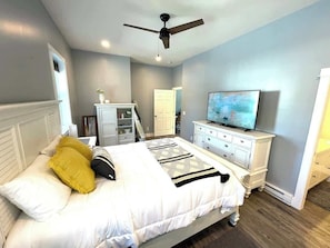 A bedroom with a bed, a television, a ceiling fan, and a dresser.