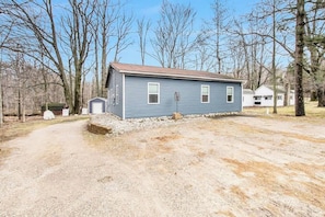 A single-story blue house with a gravel driveway, surrounded by trees.