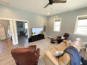 Ein Wohnzimmer mit Fernseher, Ledersesseln, einer Couch und einem Deckenventilator.