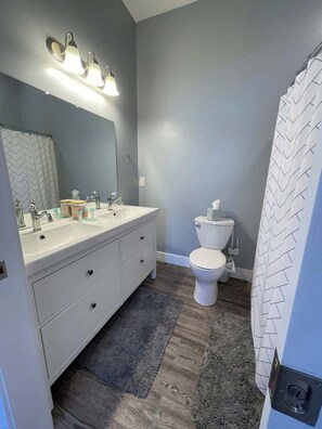 A bathroom with a grey wall, a white sink with a mirror, a toilet, and a shower curtain.