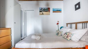 A bedroom with a wooden bed, white bedding, a wooden dresser, and two wall-mounted pictures.