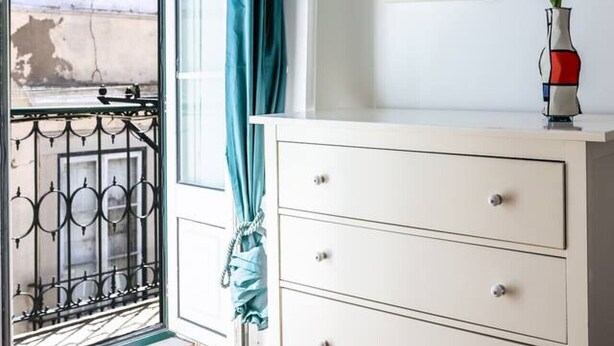 A bedroom with a bed, a white dresser, a painting, and a vase with flowers.