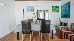 A dining area with a table set for two, two chairs, a vase with red flowers, and a green side table with a sign.