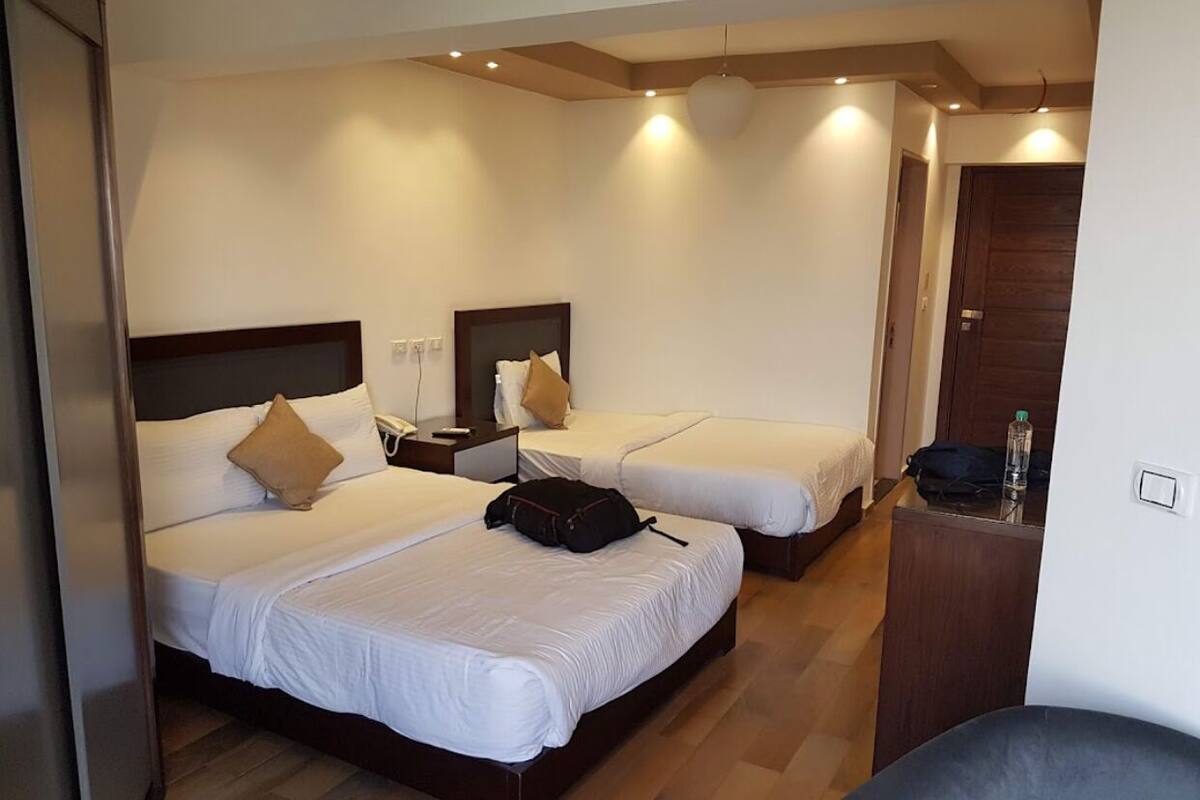 A hotel room with two beds, each with a headboard, bedside tables, and a lamp.