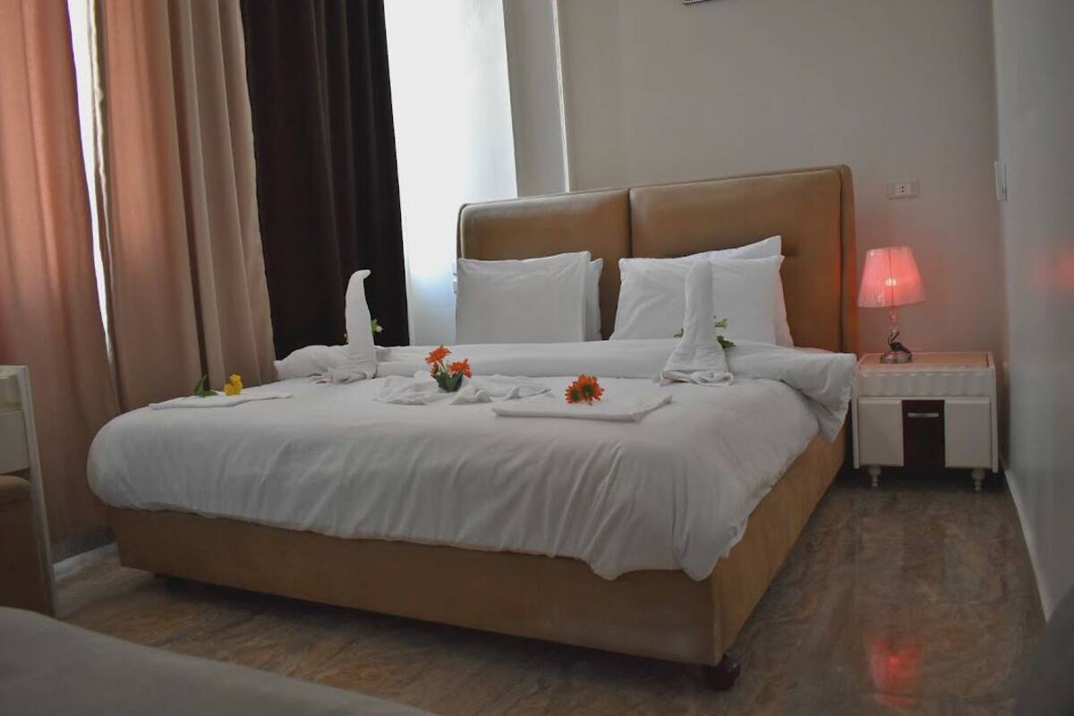 A neatly made bed with white linens, a bedside lamp, and a tray with flowers.