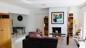 Una sala moderna con un sofá marrón oscuro, un aparador de madera, una mesa de comedor con sillas, una estantería y una chimenea.