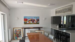 Una cocina moderna con una isla grande, un área de comedor con una mesa y sillas de madera, y un cuadro de colores sobre la mesa.