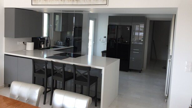 Una cocina moderna con una isla central, muebles oscuros y un refrigerador de acero inoxidable.