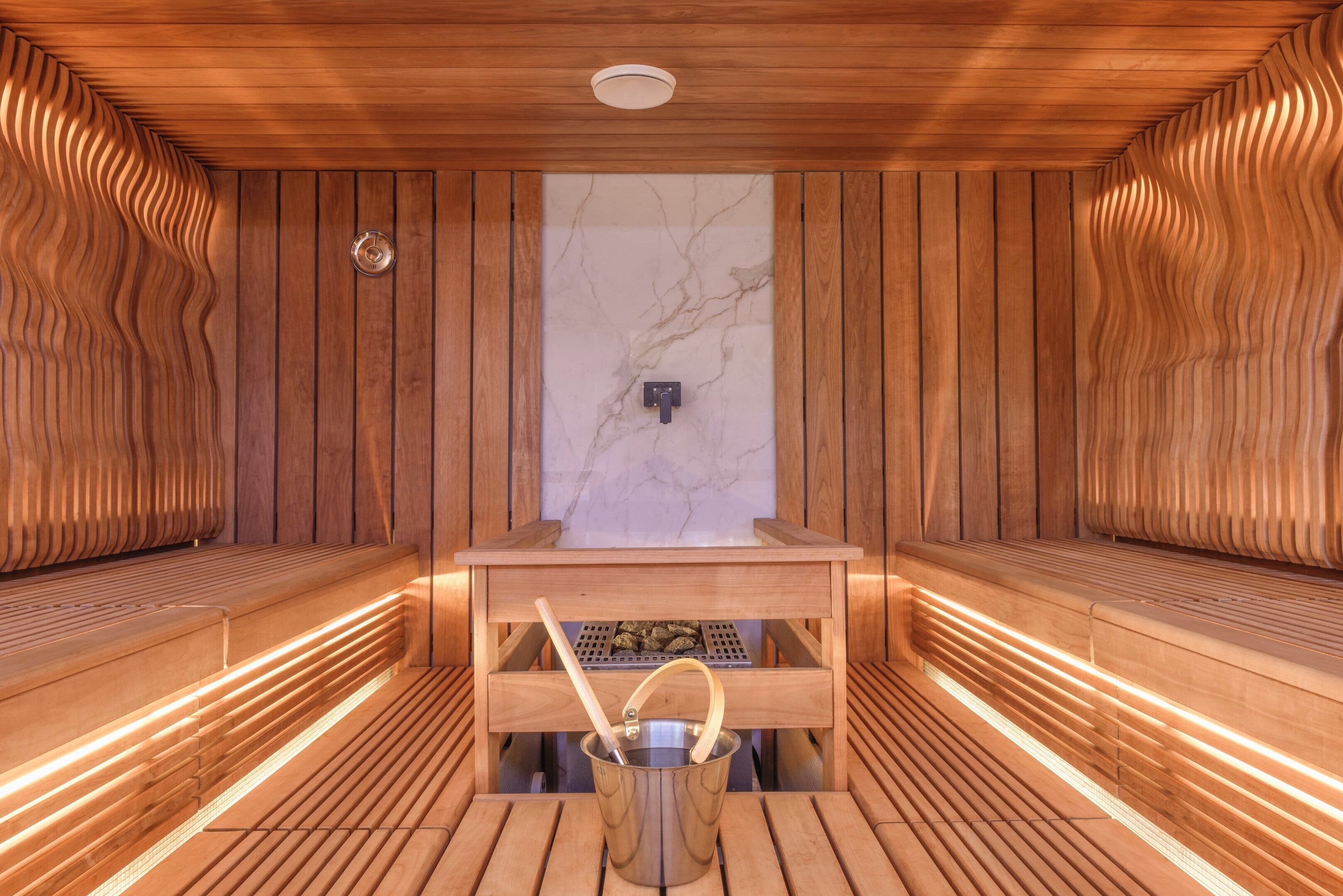 Sauna, jossa on puiset lauteet, marmoriseinä ja metallinen astia, jossa on kahva.