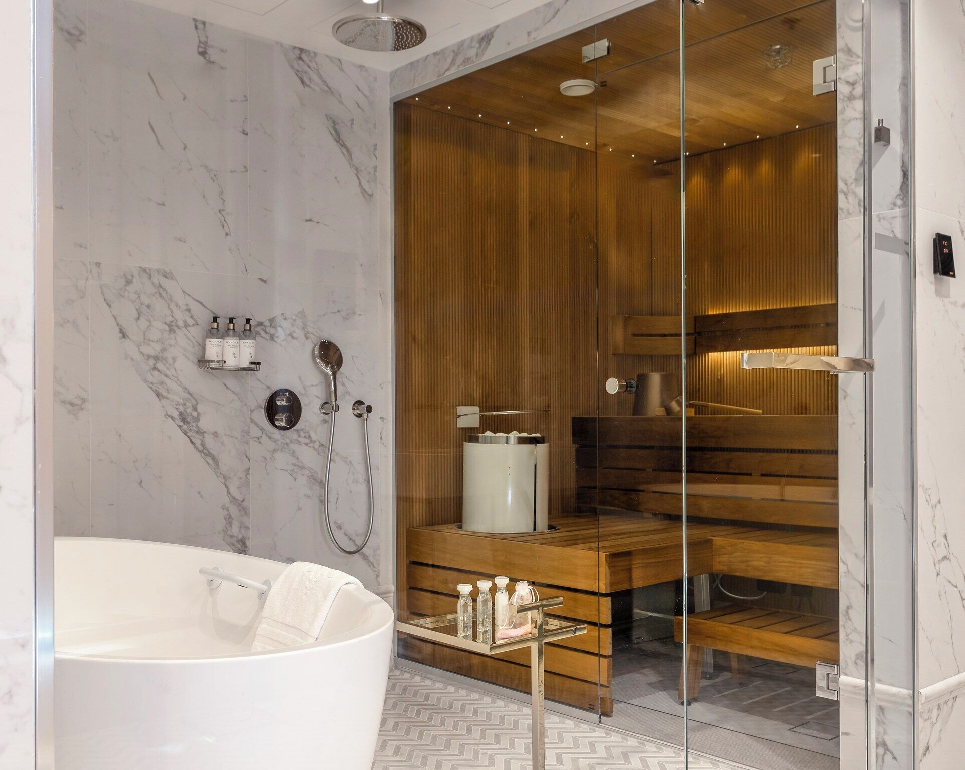 A modern bathroom with a freestanding bathtub, wooden sauna, and marble walls.