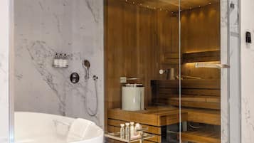 A modern bathroom with a freestanding bathtub, wooden sauna, and marble walls.