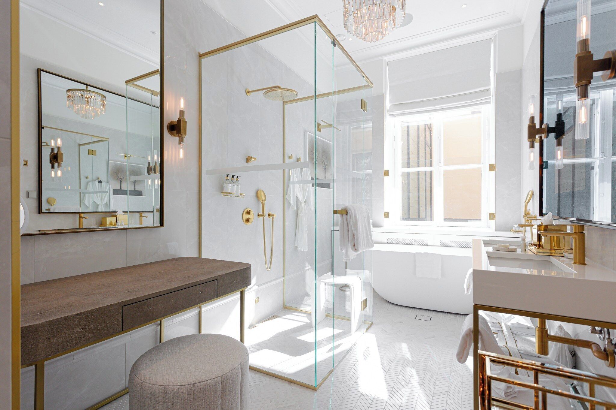 A luxurious bathroom with a glass-enclosed shower, a large mirror, and a vanity with gold fixtures.