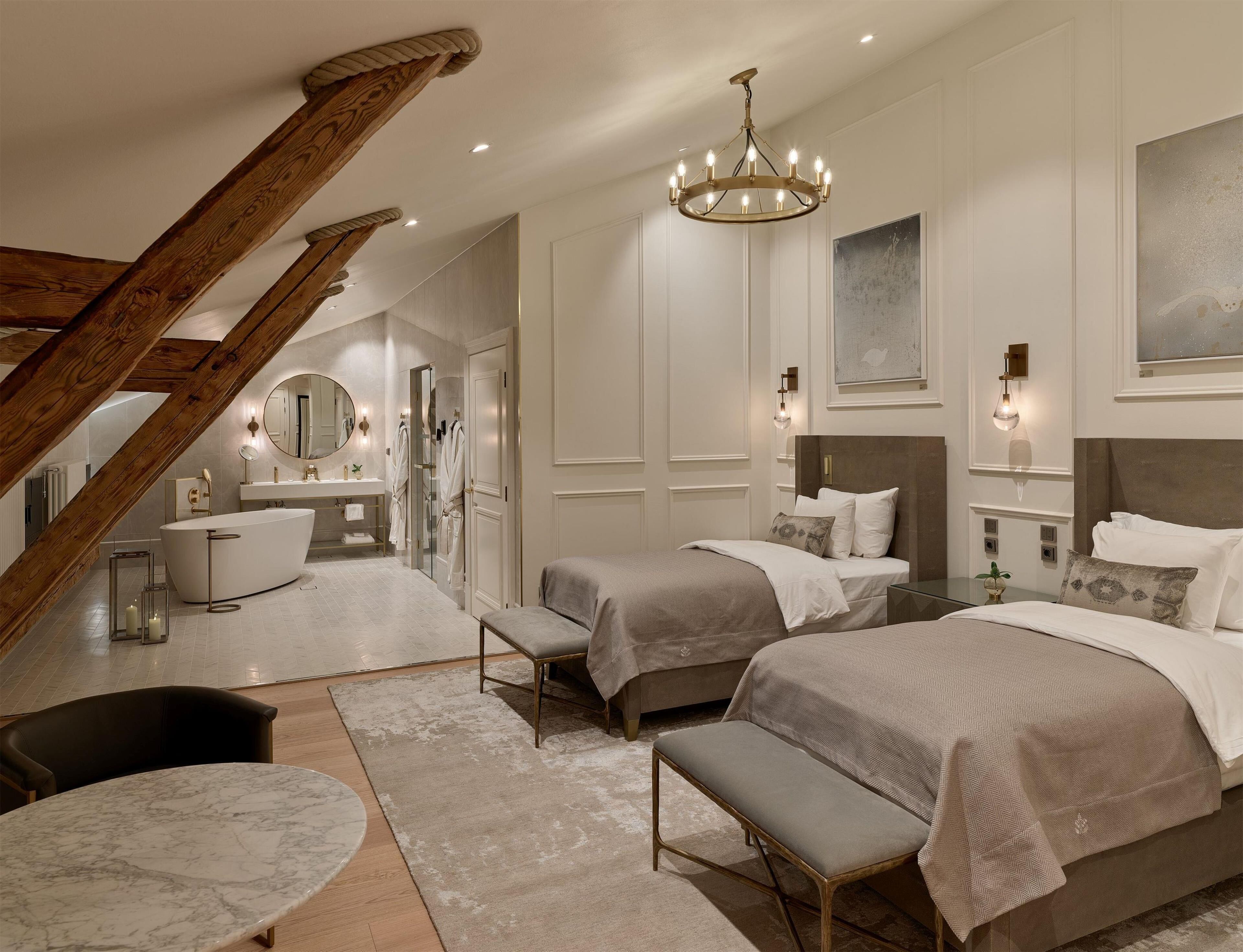 A modern bedroom with a large bed, a smaller bed, a bench, a chair, and a vanity with a mirror.