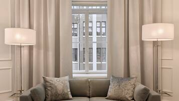 A modern living room with a beige sofa, two side tables, a glass coffee table, and a large window with curtains.