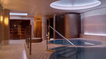Ein Wellnessbereich mit Whirlpool, einer Treppe und einer Glastür zum Sauna-Bereich.