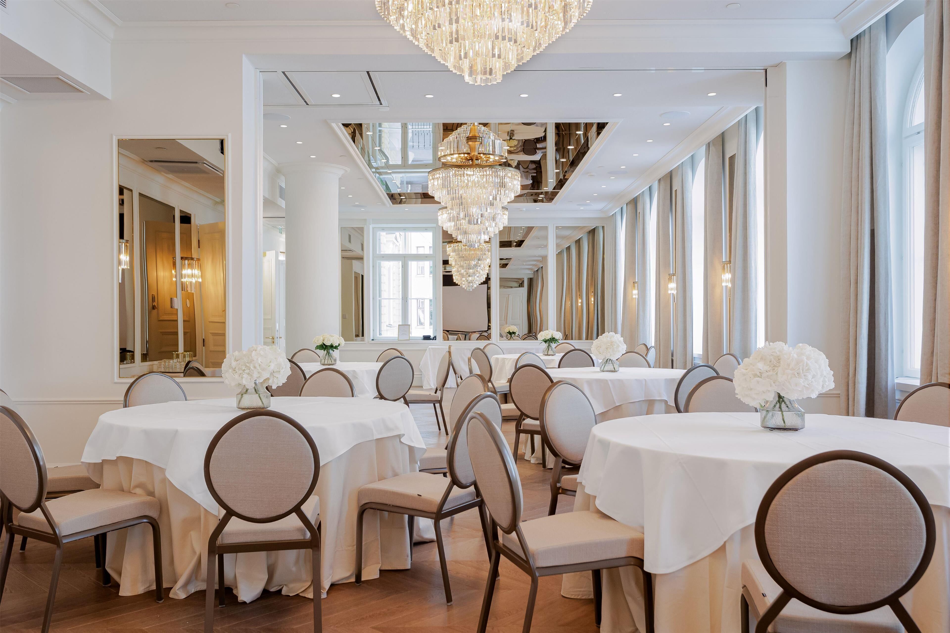 A formal dining room with multiple tables, chairs, and a large chandelier.