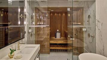 Un baño moderno con ducha envuelta en vidrio, tocador de madera y suelo de mármol.