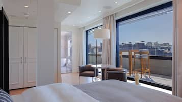 Una habitación de hotel moderna con una cama grande, un balcón con mesa y sillas, y vistas a la ciudad.